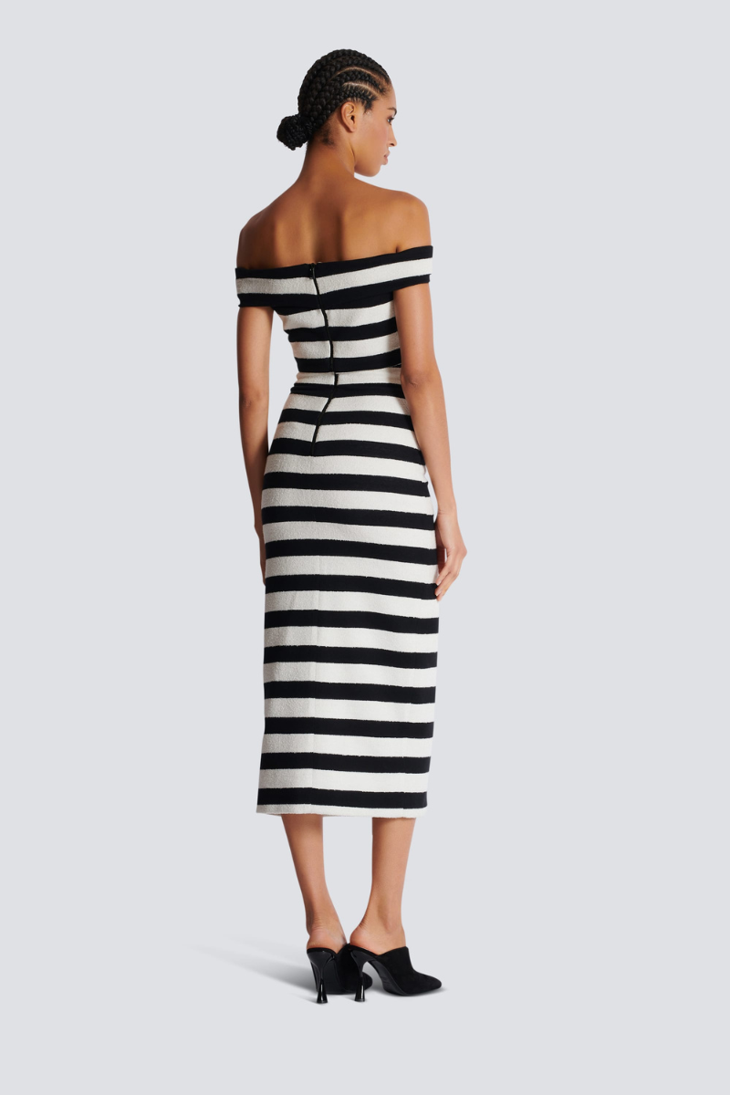 Black - Full-length side view of a model wearing a black and white striped two-piece dress, featuring an off-the-shoulder crop top and a high-waisted midi skirt with a front slit and gold buttons.