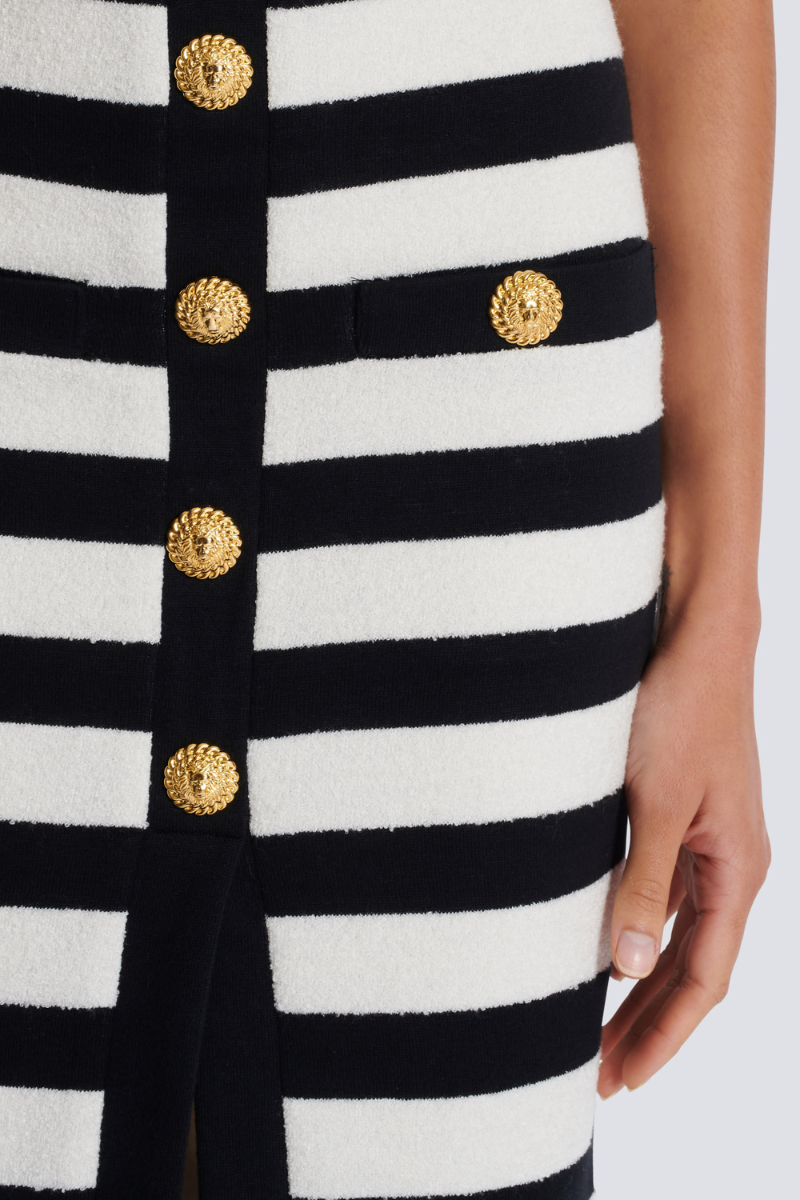 Black - Full-length side view of a model wearing a black and white striped two-piece dress, featuring an off-the-shoulder crop top and a high-waisted midi skirt with a front slit and gold buttons.