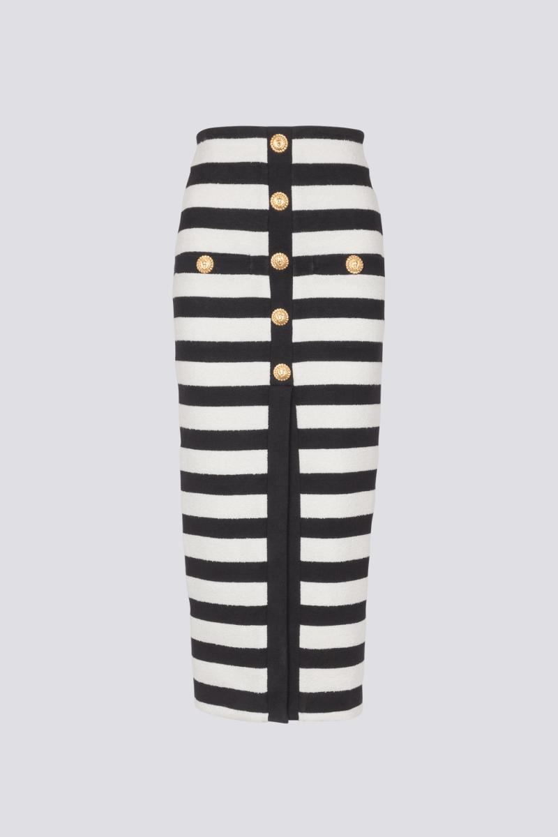 Black - Full-length side view of a model wearing a black and white striped two-piece dress, featuring an off-the-shoulder crop top and a high-waisted midi skirt with a front slit and gold buttons.