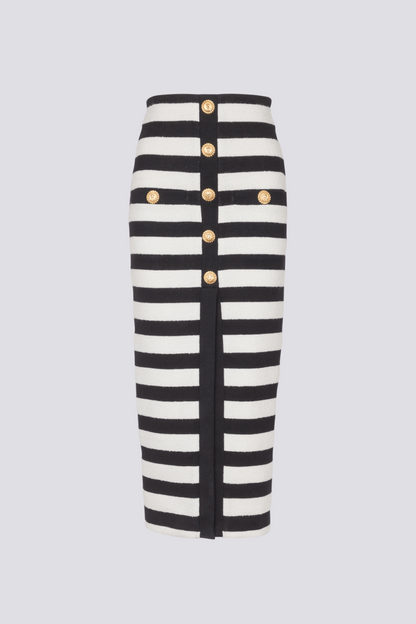 Black - Full-length side view of a model wearing a black and white striped two-piece dress, featuring an off-the-shoulder crop top and a high-waisted midi skirt with a front slit and gold buttons.