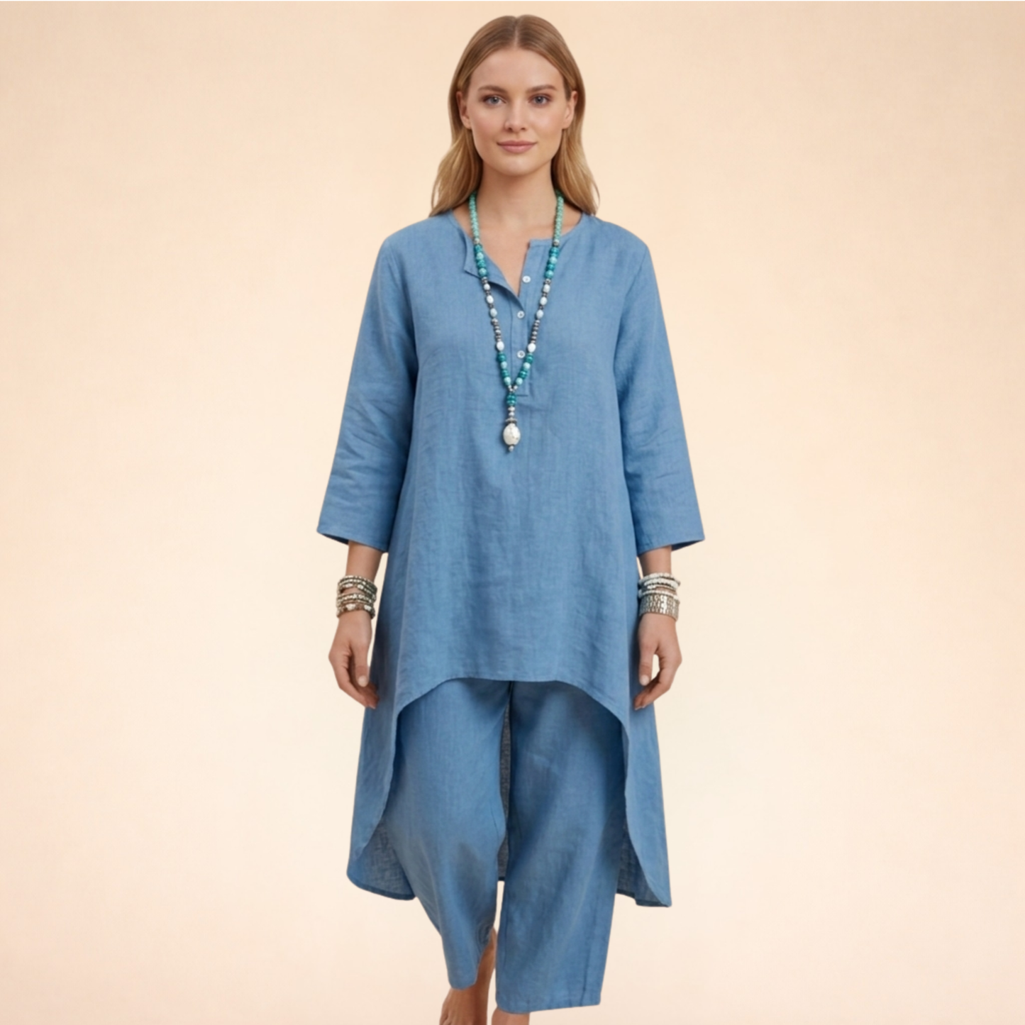 Blau - A woman modelling a light-coloured, relaxed-fit resort tunic top featuring a split neckline, three-quarter sleeves, and a dramatic high-low hemline.