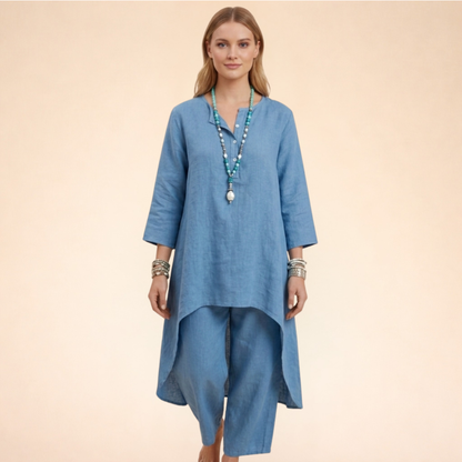Blau - A woman modelling a light-coloured, relaxed-fit resort tunic top featuring a split neckline, three-quarter sleeves, and a dramatic high-low hemline.