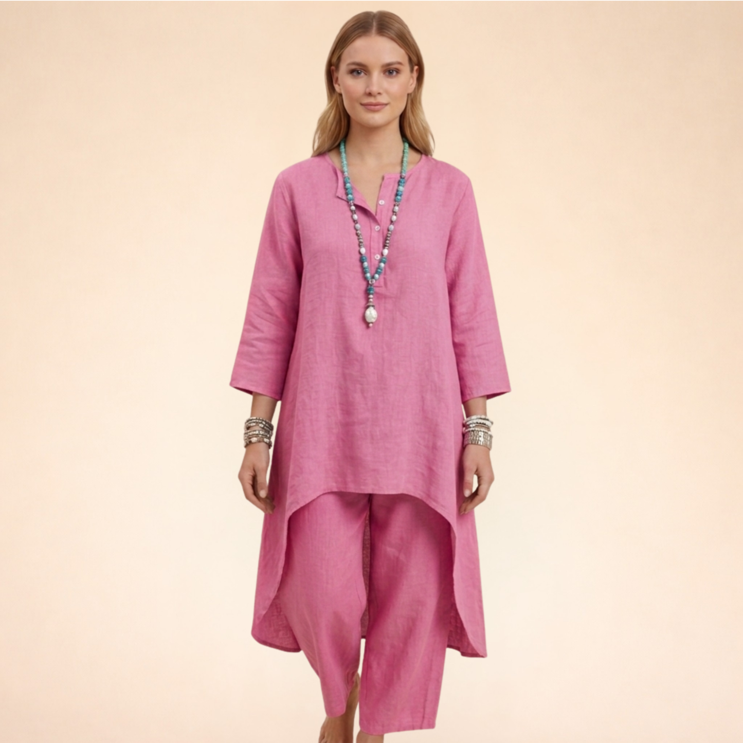 Rosa - A woman modelling a light-coloured, relaxed-fit resort tunic top featuring a split neckline, three-quarter sleeves, and a dramatic high-low hemline.