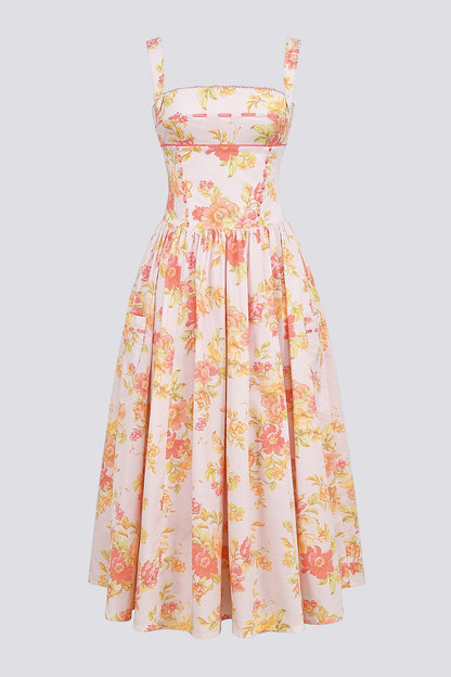 A woman stands against a light gray background wearing a floral print midi dress with a structured corset bodice, wide shoulder straps, and a full A-line skirt with her hands in the side pockets.