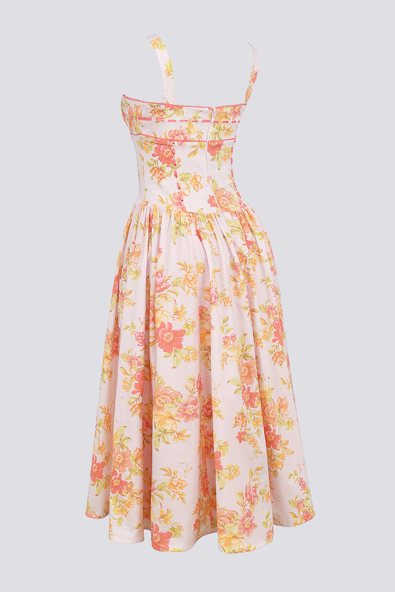 A woman stands against a light gray background wearing a floral print midi dress with a structured corset bodice, wide shoulder straps, and a full A-line skirt with her hands in the side pockets.
