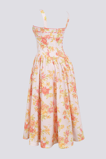 A woman stands against a light gray background wearing a floral print midi dress with a structured corset bodice, wide shoulder straps, and a full A-line skirt with her hands in the side pockets.