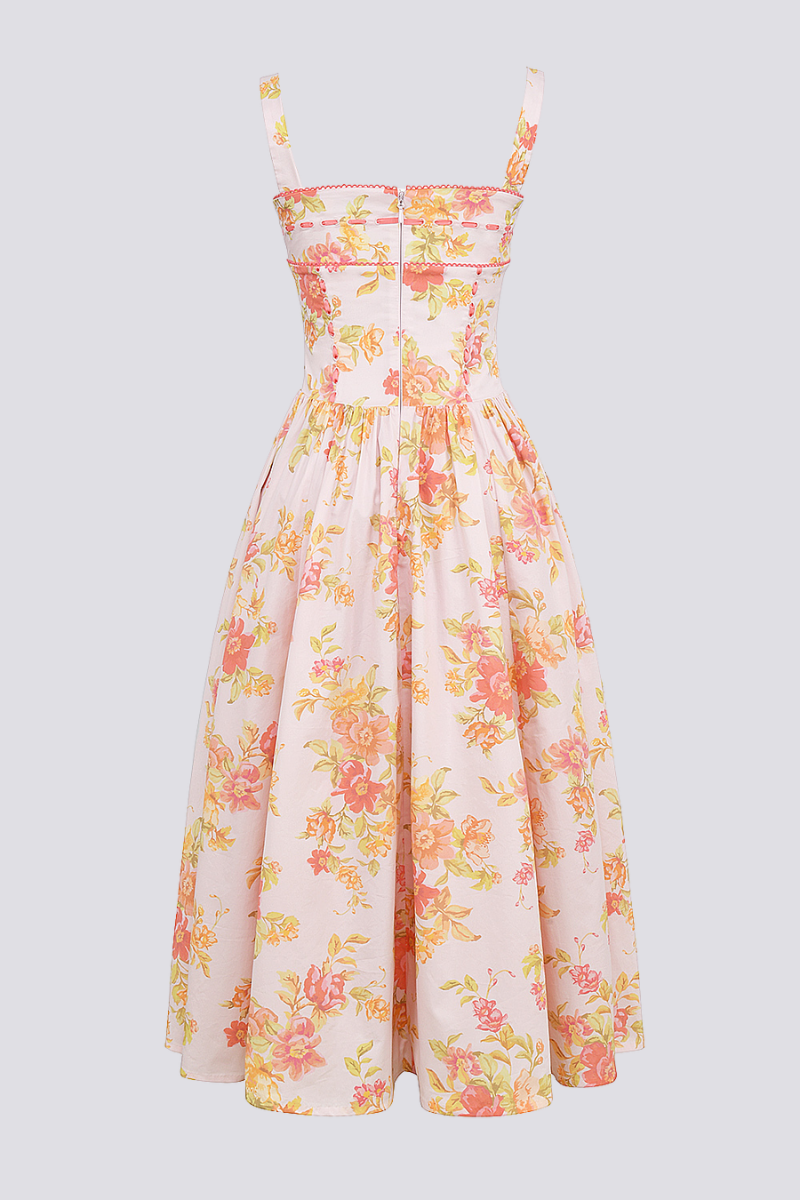 A woman stands against a light gray background wearing a floral print midi dress with a structured corset bodice, wide shoulder straps, and a full A-line skirt with her hands in the side pockets.