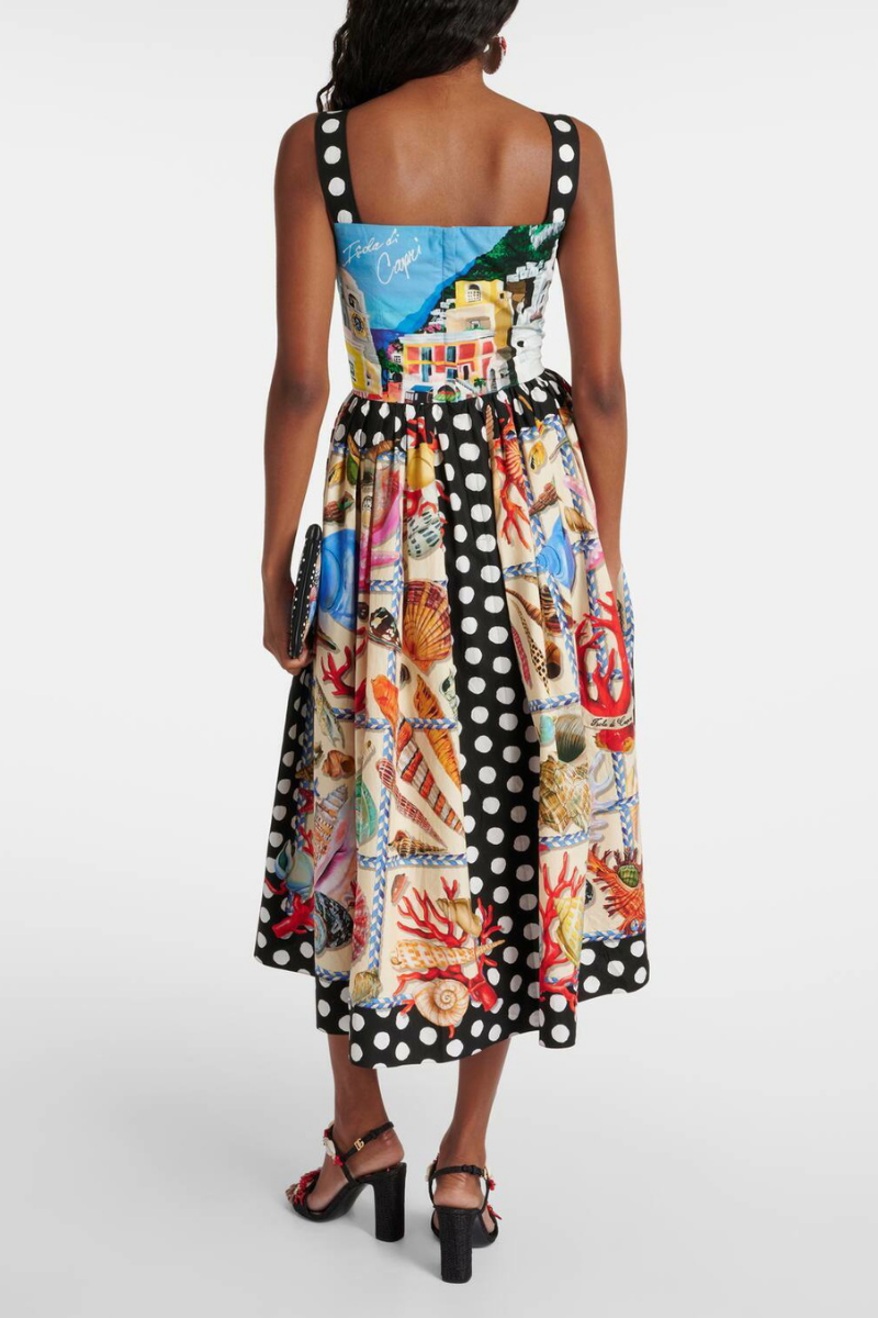 Full-length view of a woman wearing a mixed-print midi dress with a scenic-print square-neck bodice, polka dot straps, and a full A-line skirt featuring seashell and polka dot panels.