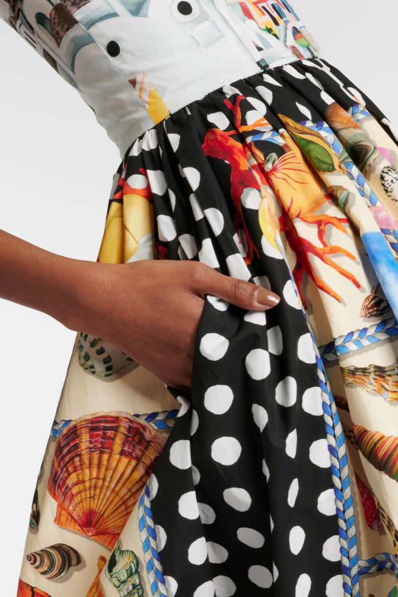Full-length view of a woman wearing a mixed-print midi dress with a scenic-print square-neck bodice, polka dot straps, and a full A-line skirt featuring seashell and polka dot panels.