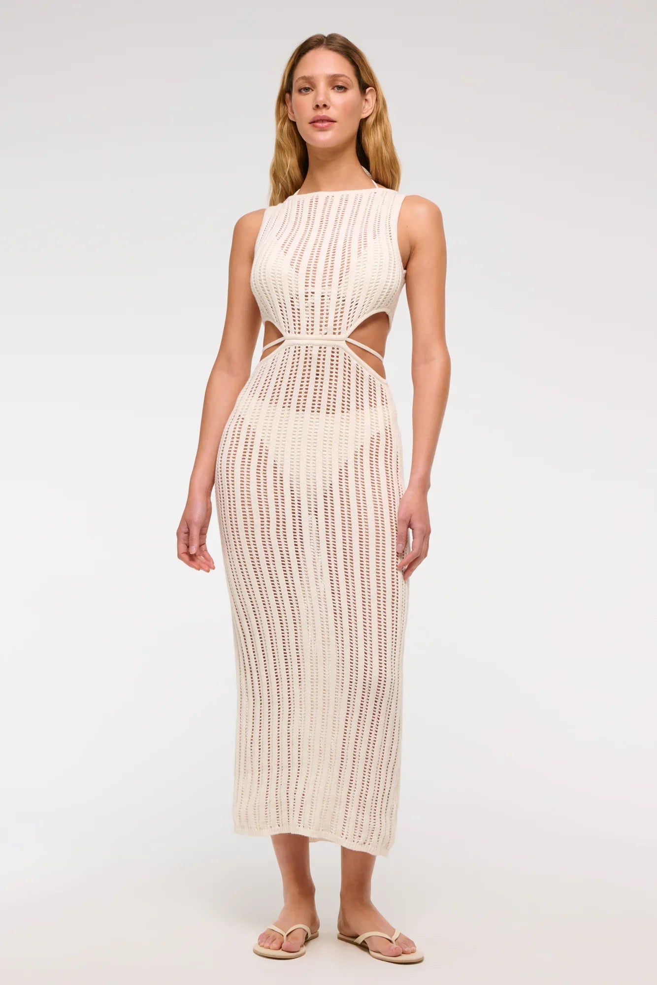White - A woman models a sleeveless, cream-colored open-knit maxi dress with a high neckline and cutouts at the waist, shown against a plain white background.