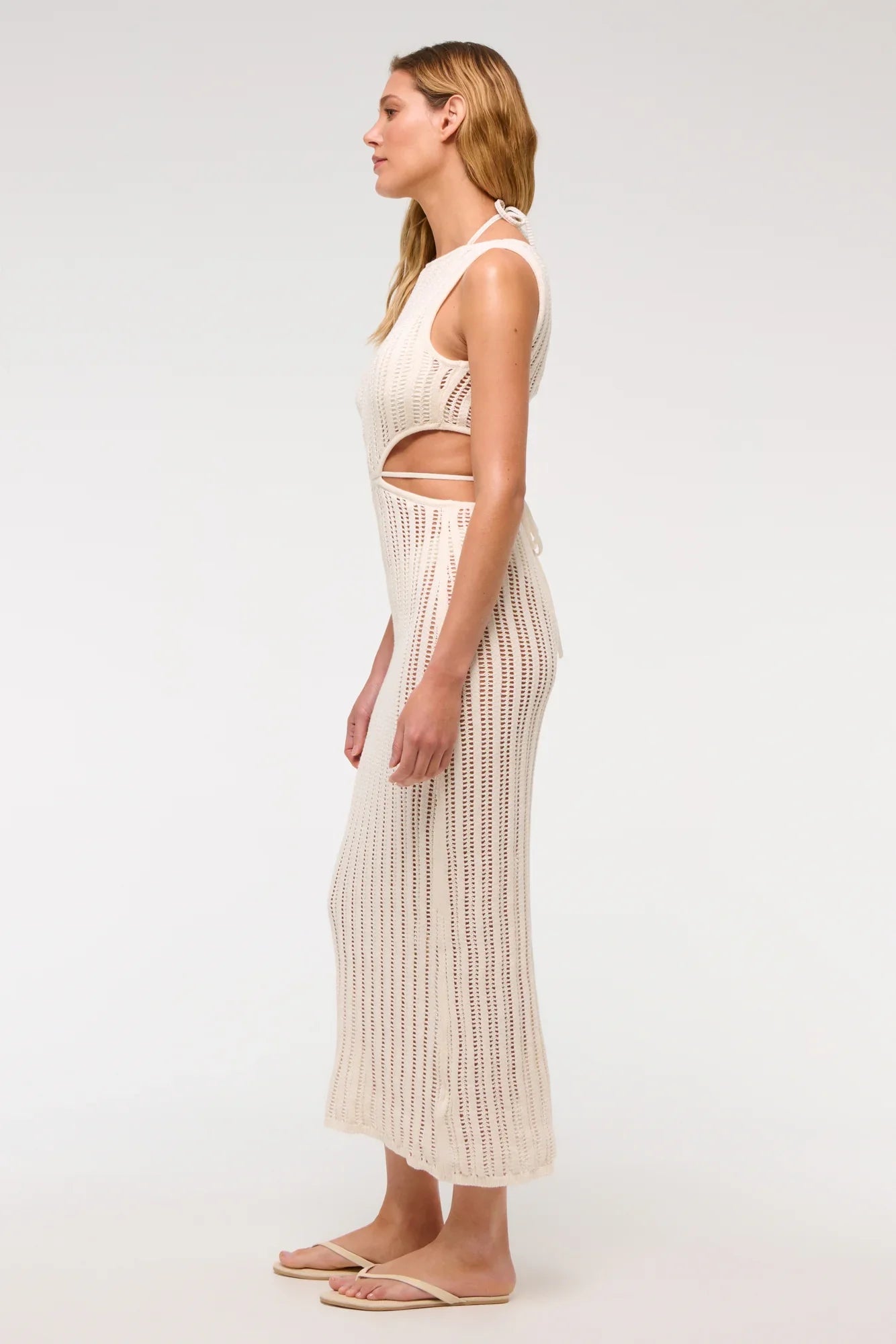 White - A woman models a sleeveless, cream-colored open-knit maxi dress with a high neckline and cutouts at the waist, shown against a plain white background.