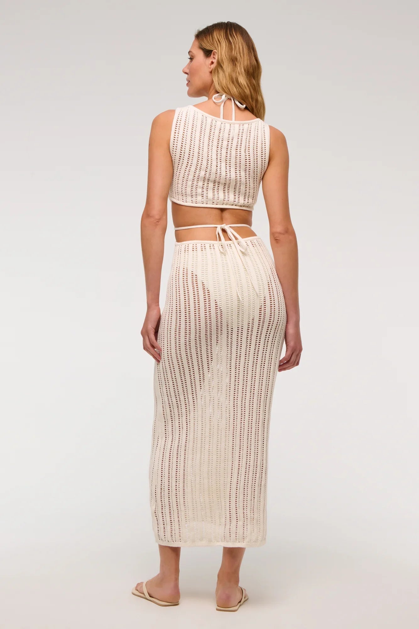 White - A woman models a sleeveless, cream-colored open-knit maxi dress with a high neckline and cutouts at the waist, shown against a plain white background.
