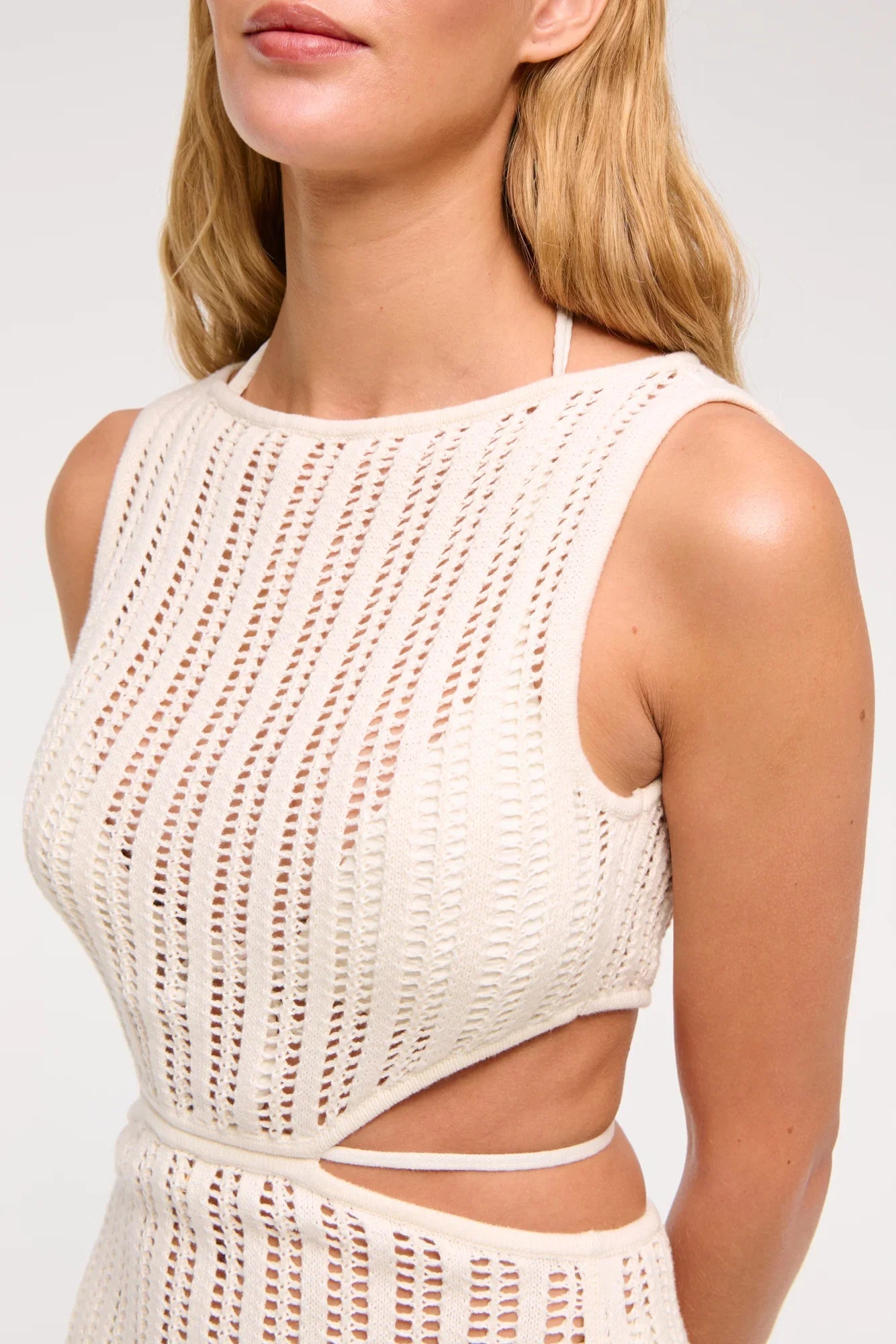 White - A woman models a sleeveless, cream-colored open-knit maxi dress with a high neckline and cutouts at the waist, shown against a plain white background.