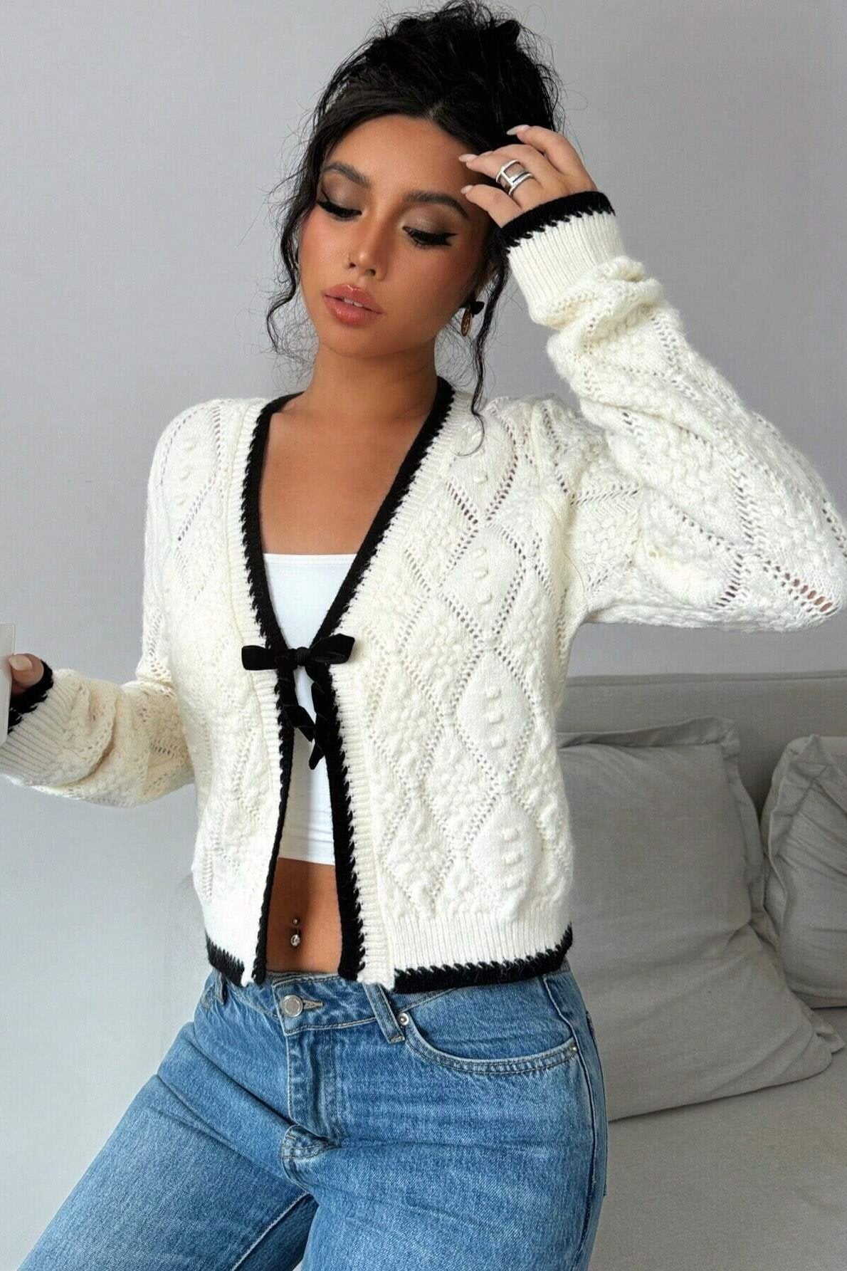 Woman in cream cable knit cardigan and flared jeans taking a selfie