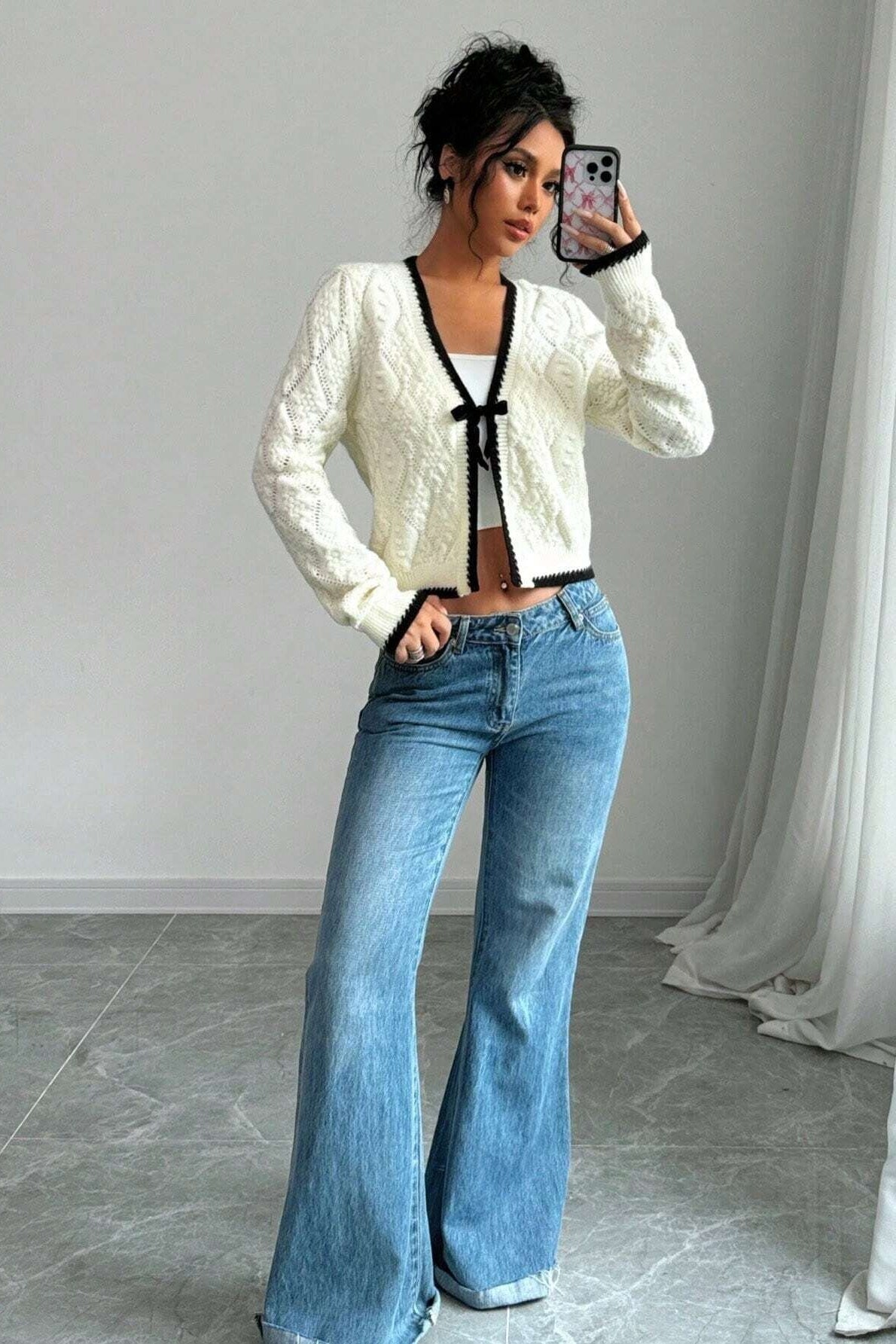 Woman in cream cable knit cardigan and flared jeans taking a selfie
