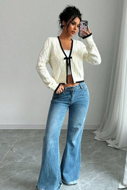 Woman in cream cable knit cardigan and flared jeans taking a selfie