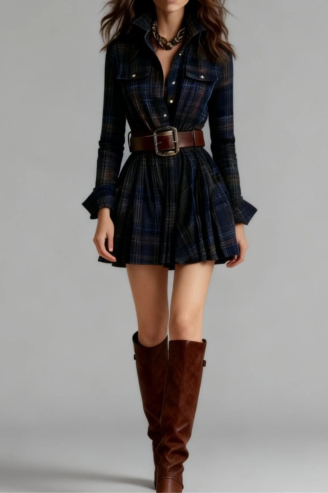 Blue - A woman models a long-sleeve, collared mini shirtdress in a multicolor plaid pattern. The dress is cinched with a wide brown belt and features a full, flared skirt, styled with tall brown boots against a grey studio background.