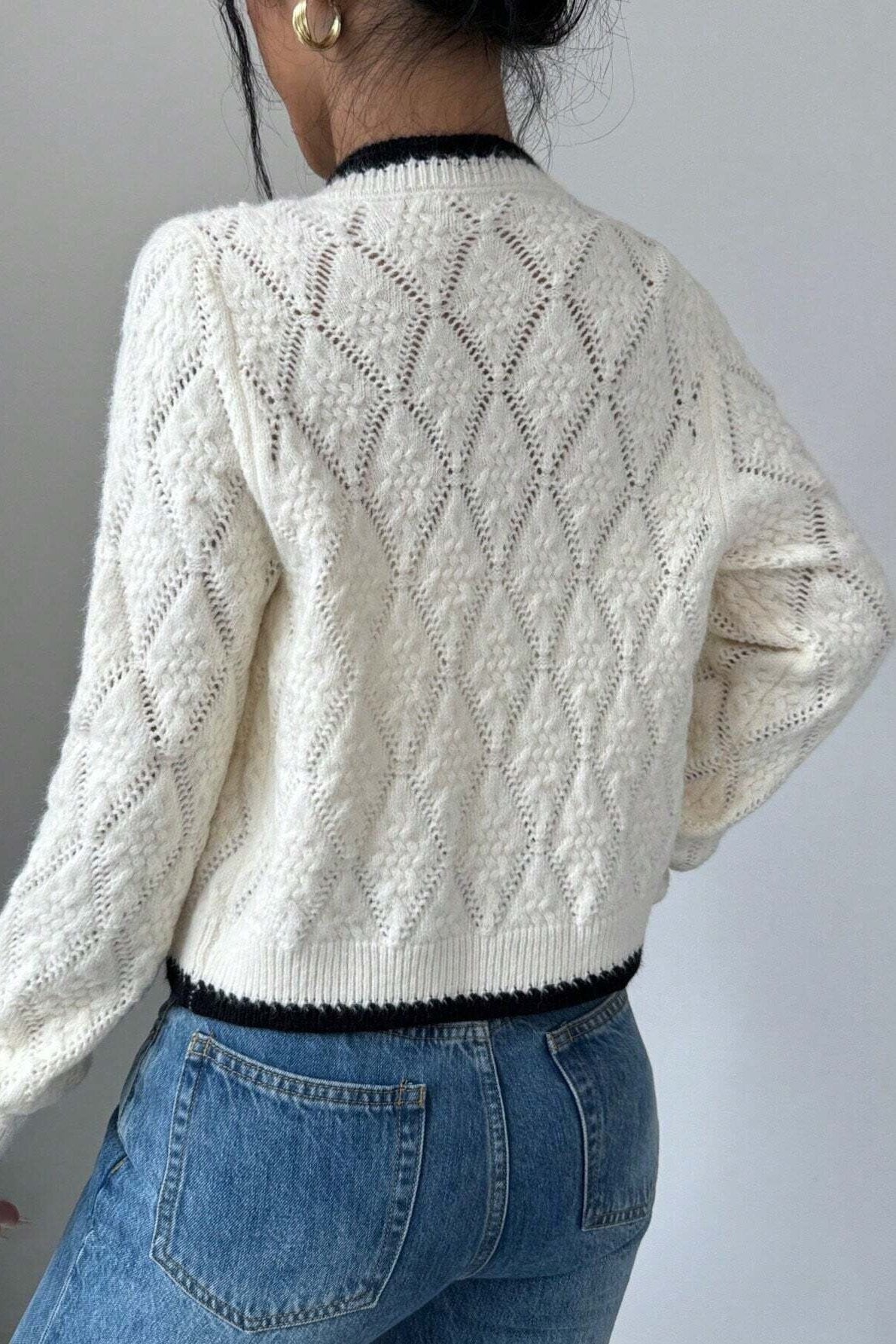 Woman in cream cable knit cardigan and flared jeans taking a selfie