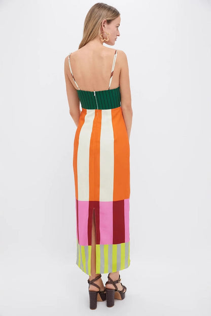 A full-length shot of a woman modeling a sleeveless midi dress with spaghetti straps. The dress has a straight, column silhouette and features a vibrant, multi-colored pattern of vertical stripes and color-blocked panels at the bodice and hem.