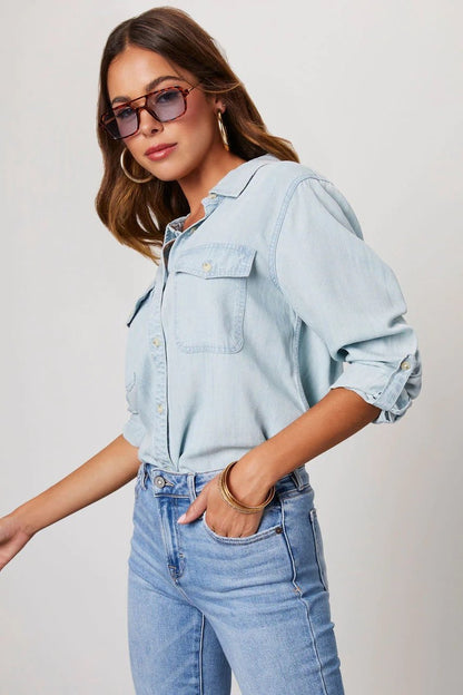 Light Blue - Women's light blue denim button-down shirt featuring a point collar, dual chest flap pockets, and rolled sleeves secured with button tabs, styled casually.