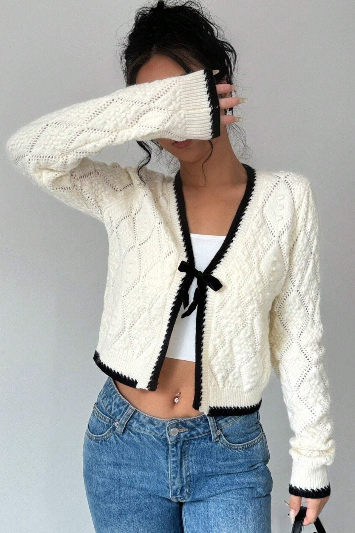 Woman in cream cable knit cardigan and flared jeans taking a selfie