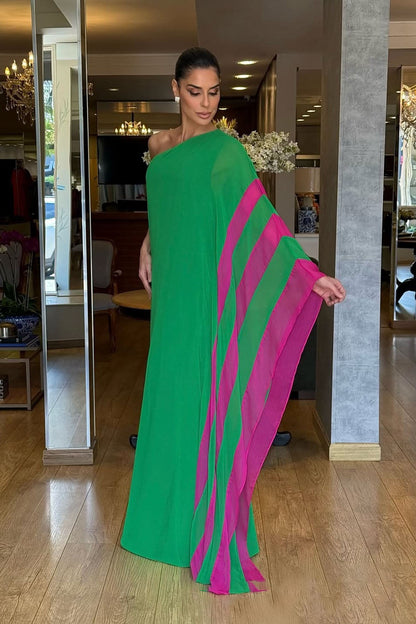 A woman models a vibrant green, one-shoulder, floor-length gown against a white background. The gown has a dramatic, flowing sleeve with a bright pink contrasting interior panel.
