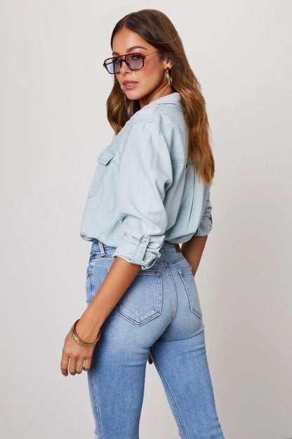Light Blue - Women's light blue denim button-down shirt featuring a point collar, dual chest flap pockets, and rolled sleeves secured with button tabs, styled casually.