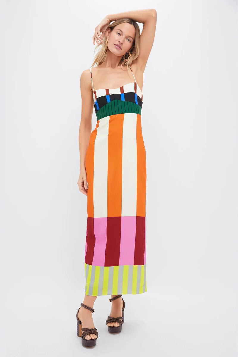 A full-length shot of a woman modeling a sleeveless midi dress with spaghetti straps. The dress has a straight, column silhouette and features a vibrant, multi-colored pattern of vertical stripes and color-blocked panels at the bodice and hem.