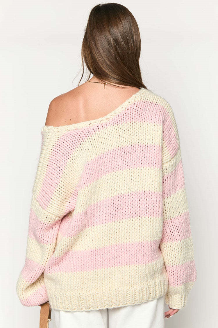 Pink - Woman wearing a chunky knit, slouchy off-shoulder jumper featuring wide horizontal stripes, paired with light wash denim jeans.