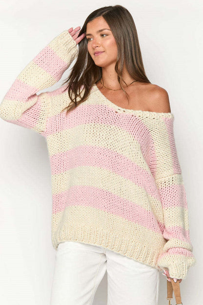 Pink - Woman wearing a chunky knit, slouchy off-shoulder jumper featuring wide horizontal stripes, paired with light wash denim jeans.