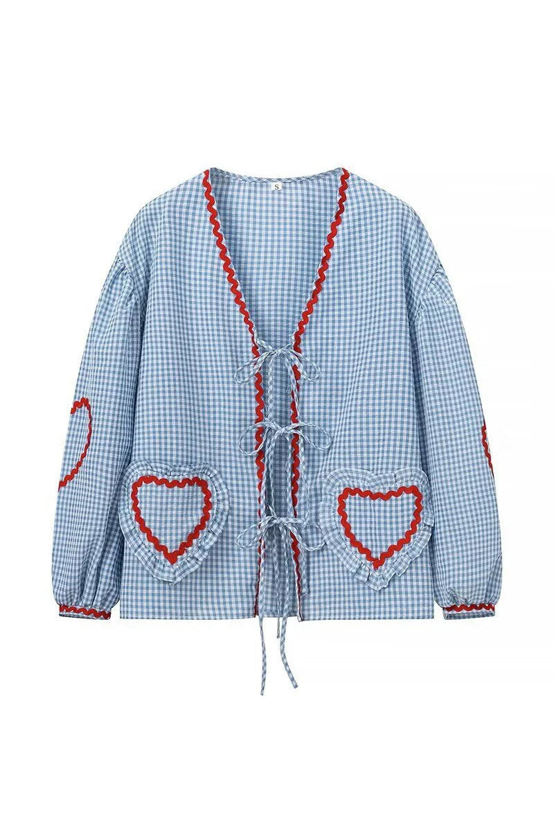 Blue - Women's pink and white gingham tie-front blouse featuring long sleeves, contrast red scalloped trim, and playful heart-shaped appliqués, styled with light wash denim shorts.