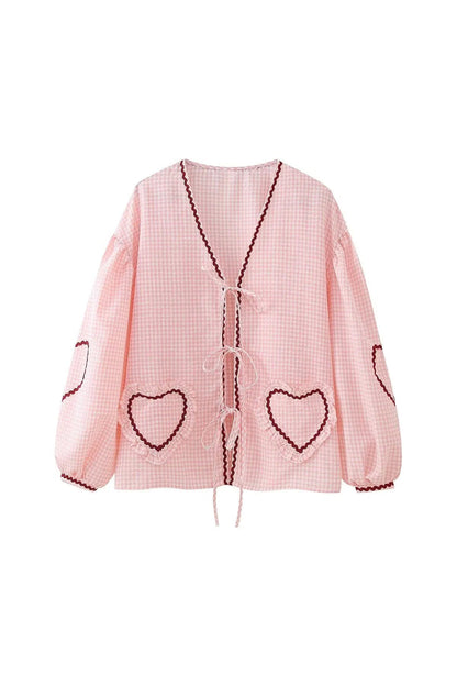 Blue - Women's pink and white gingham tie-front blouse featuring long sleeves, contrast red scalloped trim, and playful heart-shaped appliqués, styled with light wash denim shorts.