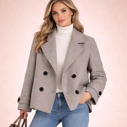 Grau - A woman wearing a camel-coloured, double-breasted cropped jacket with wide lapels and dark buttons, styled over a white turtleneck and blue jeans.