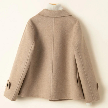 Beige - A woman wearing a camel-coloured, double-breasted cropped jacket with wide lapels and dark buttons, styled over a white turtleneck and blue jeans.