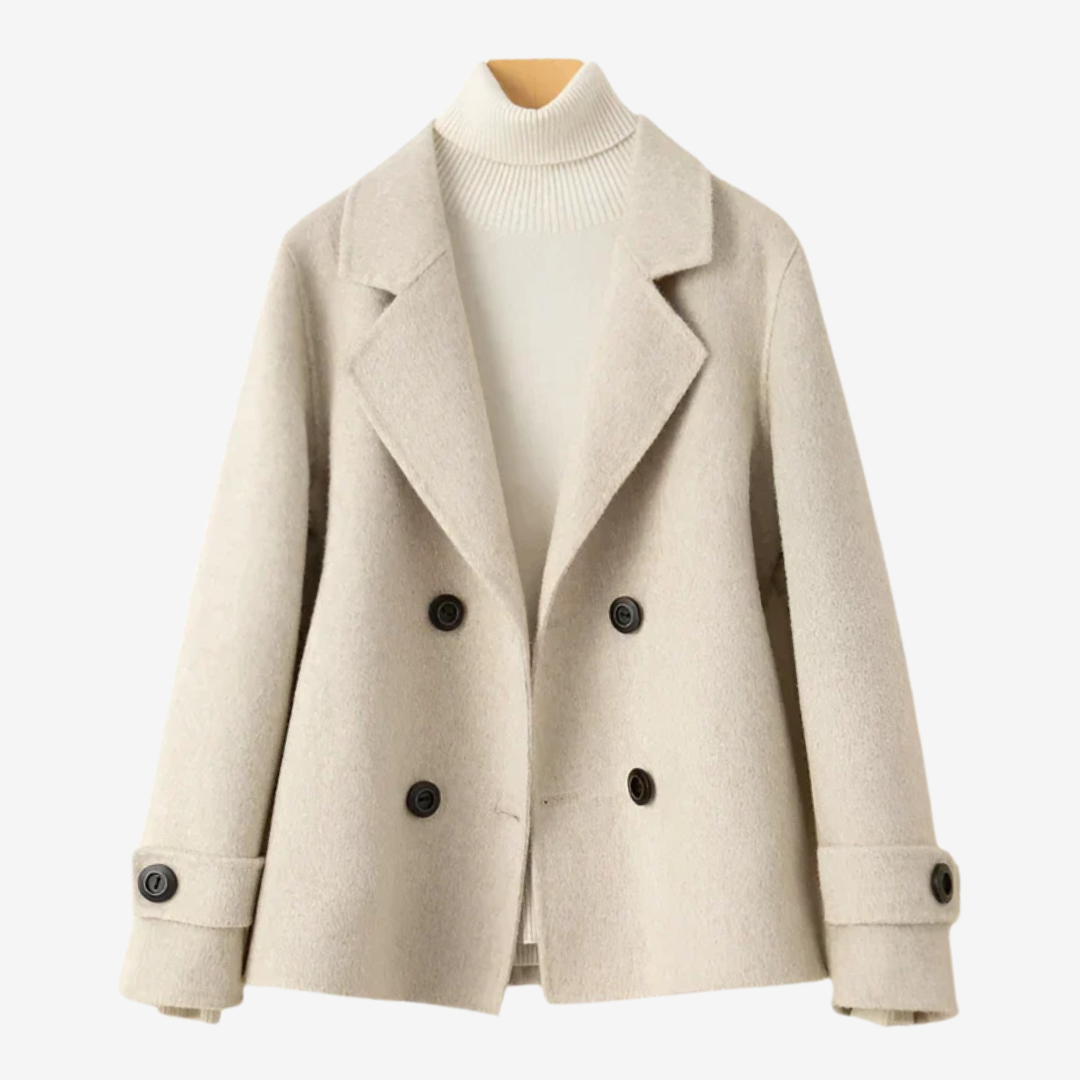 Beige - A woman wearing a camel-coloured, double-breasted cropped jacket with wide lapels and dark buttons, styled over a white turtleneck and blue jeans.