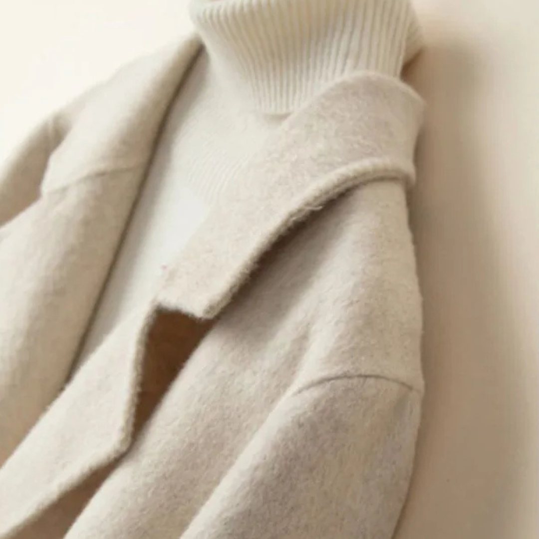 Beige - A woman wearing a camel-coloured, double-breasted cropped jacket with wide lapels and dark buttons, styled over a white turtleneck and blue jeans.