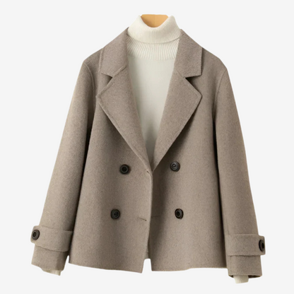Beige - A woman wearing a camel-coloured, double-breasted cropped jacket with wide lapels and dark buttons, styled over a white turtleneck and blue jeans.