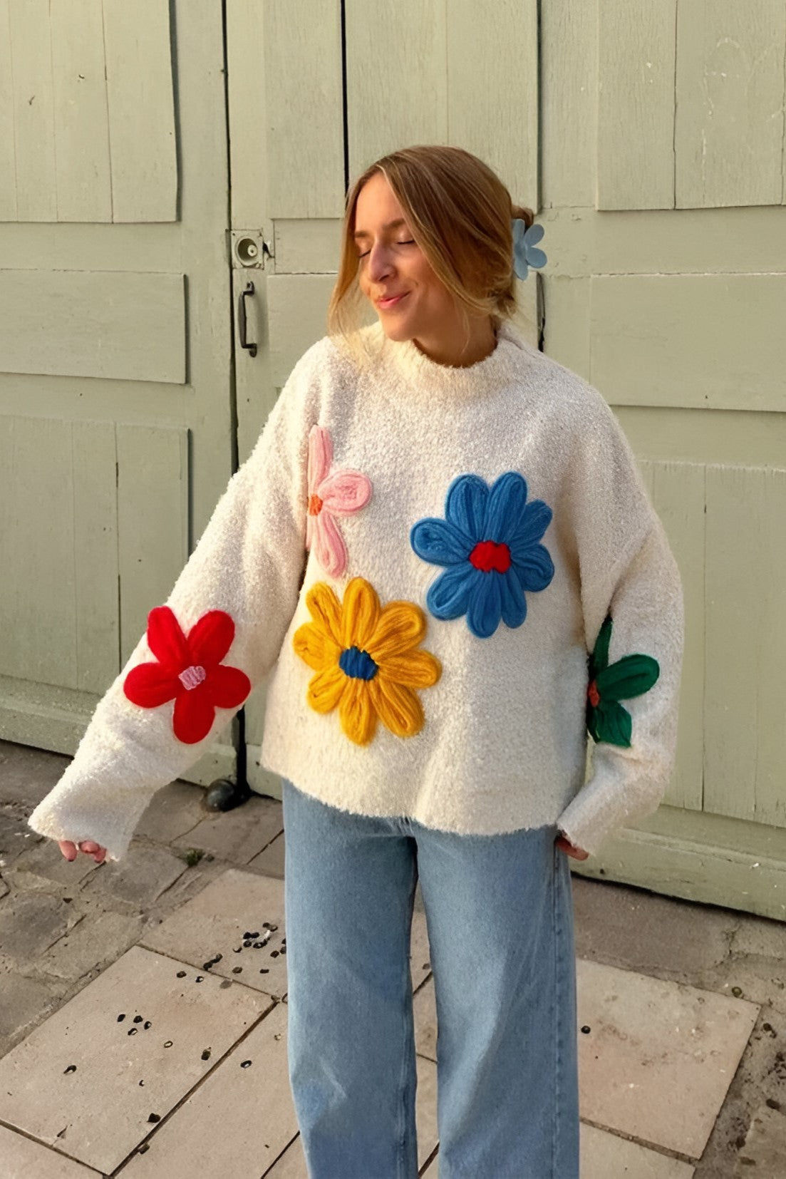 Women's fluffy cream mock neck jumper featuring oversized, colourful 3D yarn floral appliqués on the front and sleeves, styled with loose light-wash denim jeans.