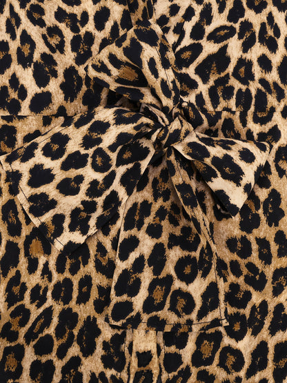 Brown - A woman wearing a long-sleeved, collared, tie-front blouse in a brown and black leopard print, paired with black pants.