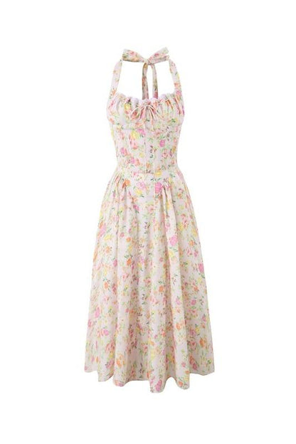 Pink - A woman with her hair in an updo smiles as she twirls in a sunlit garden, wearing a pink floral print halterneck midi dress with a corset-style ruched bodice and a full, flared skirt.