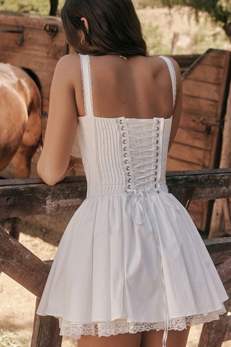 A woman stands in a sunlit vineyard wearing a vibrant red mini dress featuring a structured corset bodice, a ruched sweetheart neckline with a tie-front, wide shirred straps, and a full, flared skirt.