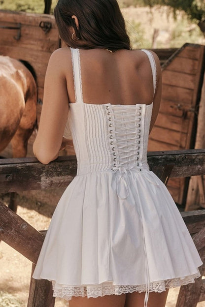 A woman stands in a sunlit vineyard wearing a vibrant red mini dress featuring a structured corset bodice, a ruched sweetheart neckline with a tie-front, wide shirred straps, and a full, flared skirt.
