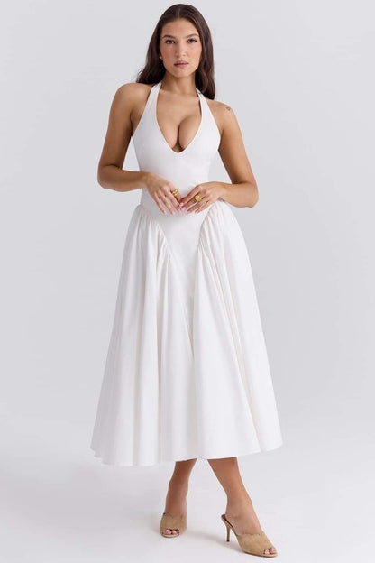 A woman models a white halter midi dress with a plunging neckline and a voluminous full skirt in an outdoor garden setting.