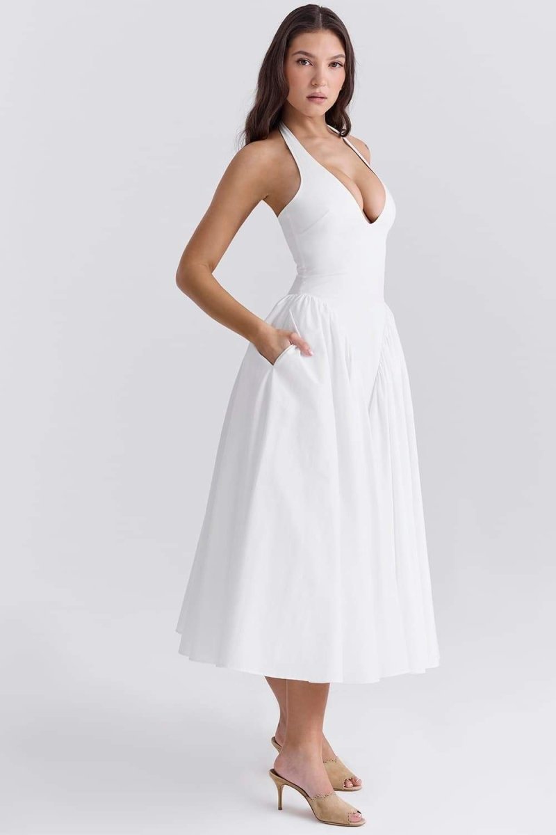 A woman models a white halter midi dress with a plunging neckline and a voluminous full skirt in an outdoor garden setting.