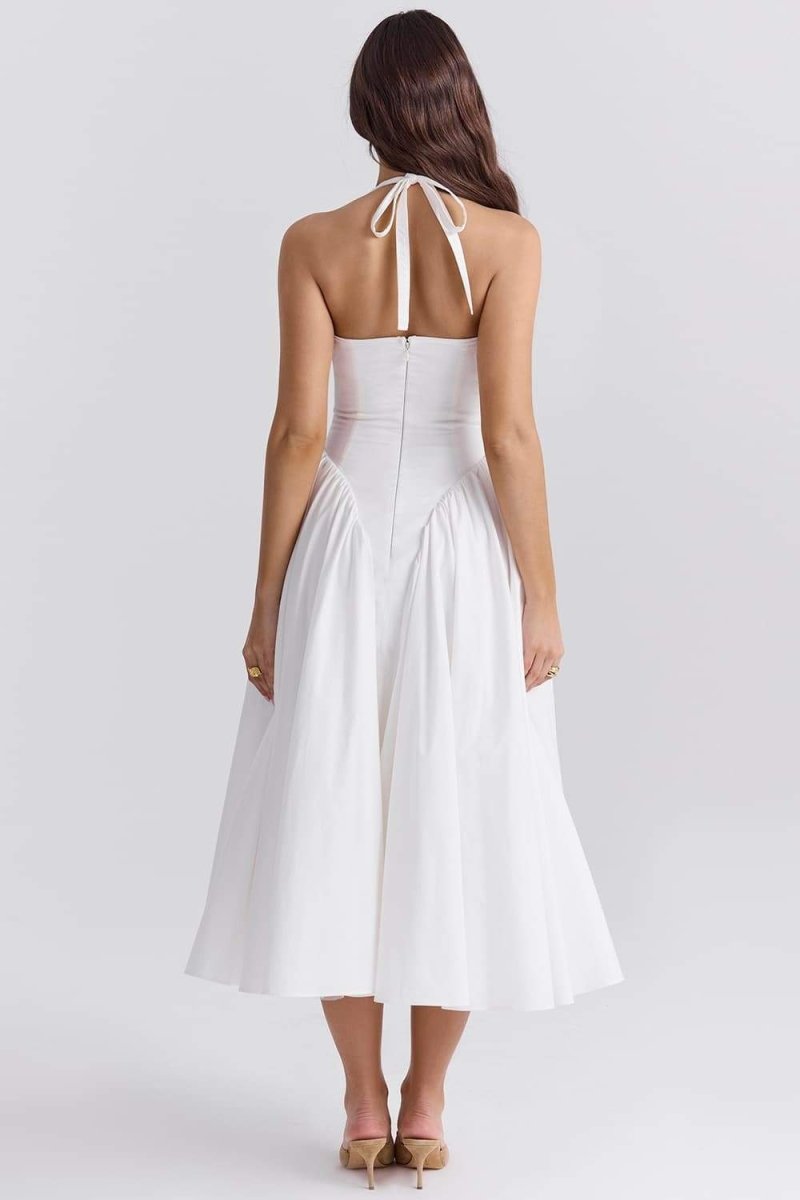 A woman models a white halter midi dress with a plunging neckline and a voluminous full skirt in an outdoor garden setting.