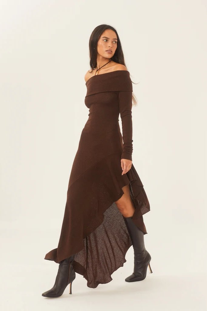 Brown - A woman models a long-sleeved, off-the-shoulder midi dress in a rich chocolate brown. The dress features a form-fitting bodice and a dramatic asymmetrical hemline with cascading ruffles, styled with black high-heeled boots.