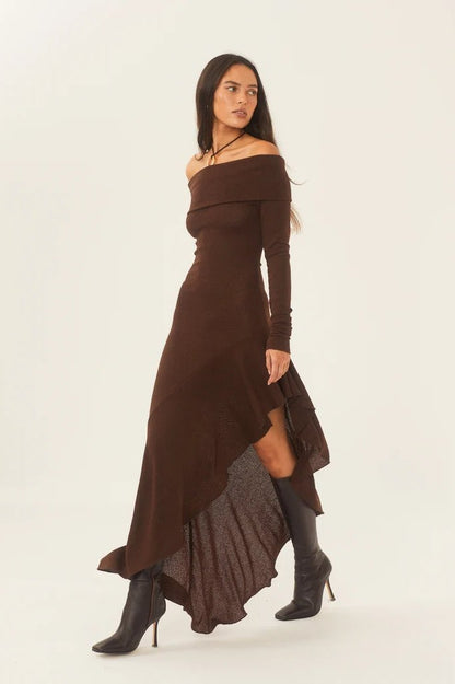 Brown - A woman models a long-sleeved, off-the-shoulder midi dress in a rich chocolate brown. The dress features a form-fitting bodice and a dramatic asymmetrical hemline with cascading ruffles, styled with black high-heeled boots.
