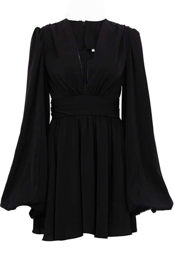 A woman with her hair in a sleek bun models a black mini dress with a plunging V-neckline, extremely voluminous long sleeves, a wide fitted waistband, and a short, flared skirt.