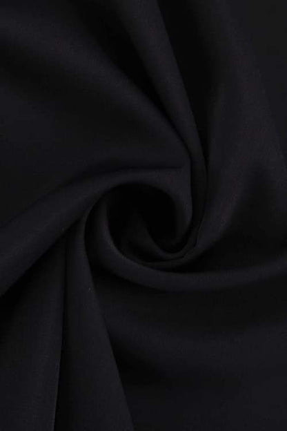 A woman with her hair in a sleek bun models a black mini dress with a plunging V-neckline, extremely voluminous long sleeves, a wide fitted waistband, and a short, flared skirt.