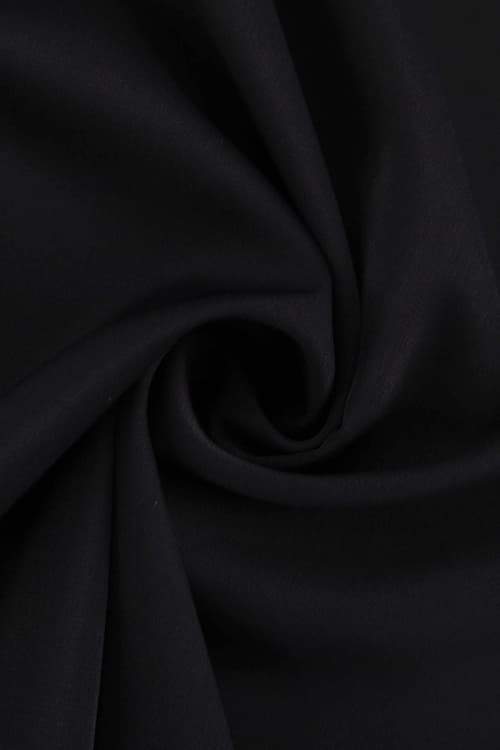 A woman with her hair in a sleek bun models a black mini dress with a plunging V-neckline, extremely voluminous long sleeves, a wide fitted waistband, and a short, flared skirt.